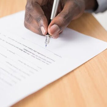 手持钢笔在桌面签署文件 Hand holding pen signing document on desk.